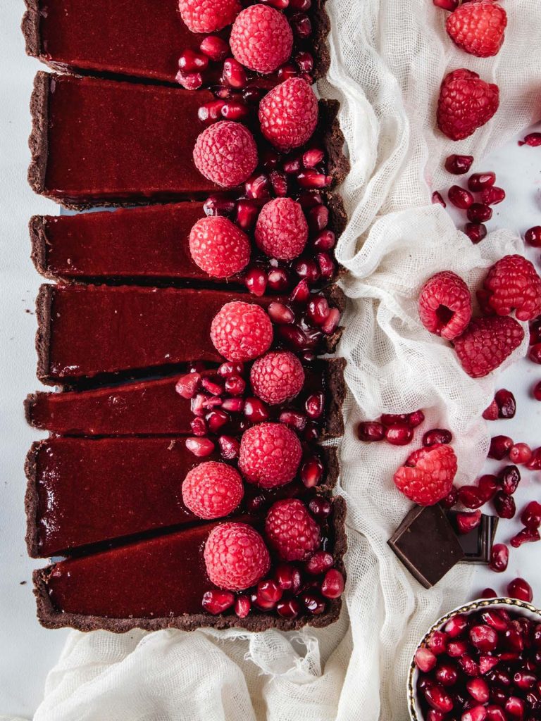 Sliced chocolate tart with pomegranate seeds and raspberries on top.