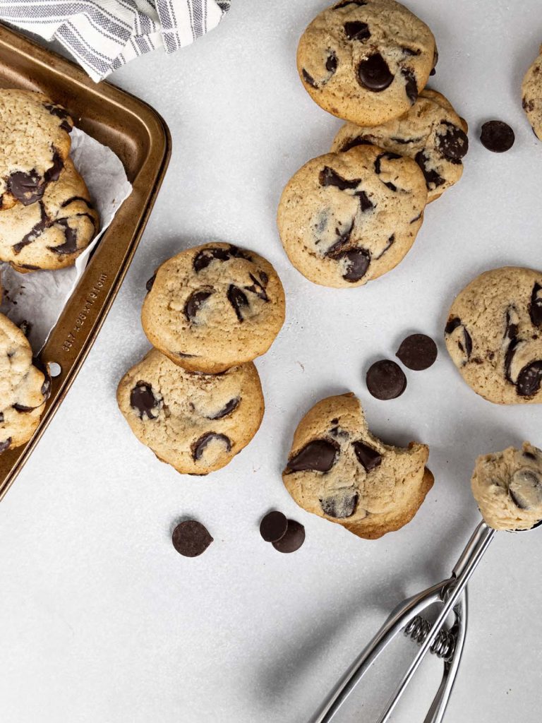 Scattered cookies on board with sheet pan and cookie scoop.