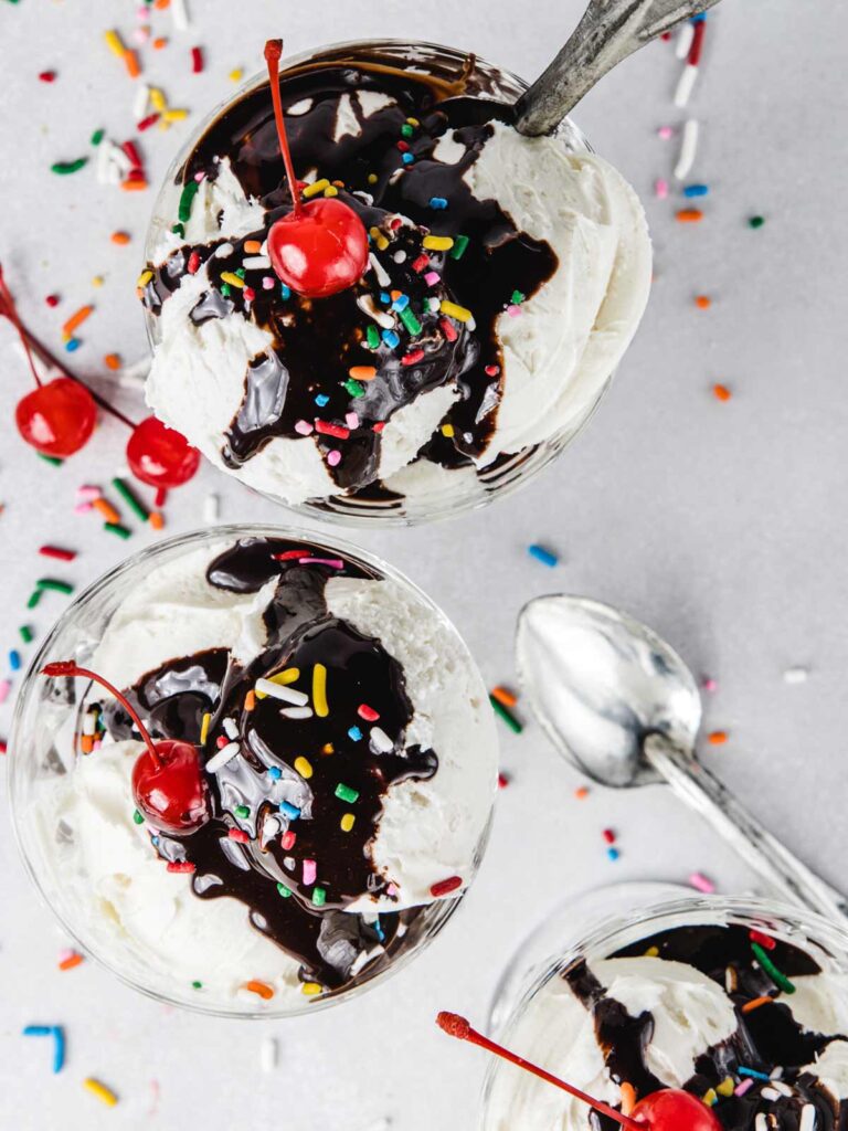 Overhead view of three ice cream sundaes with chocolate drizzled and cherries on top.