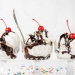 Three ice cream sundaes with chocolate syrup and cherries on top.