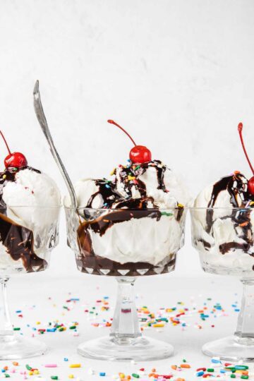 Three ice cream sundaes with chocolate syrup and cherries on top.
