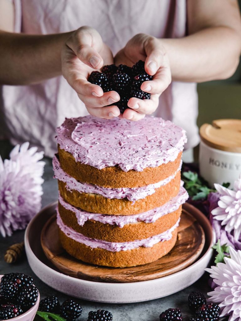 Person holding blackberries over layer cake for decorating.
