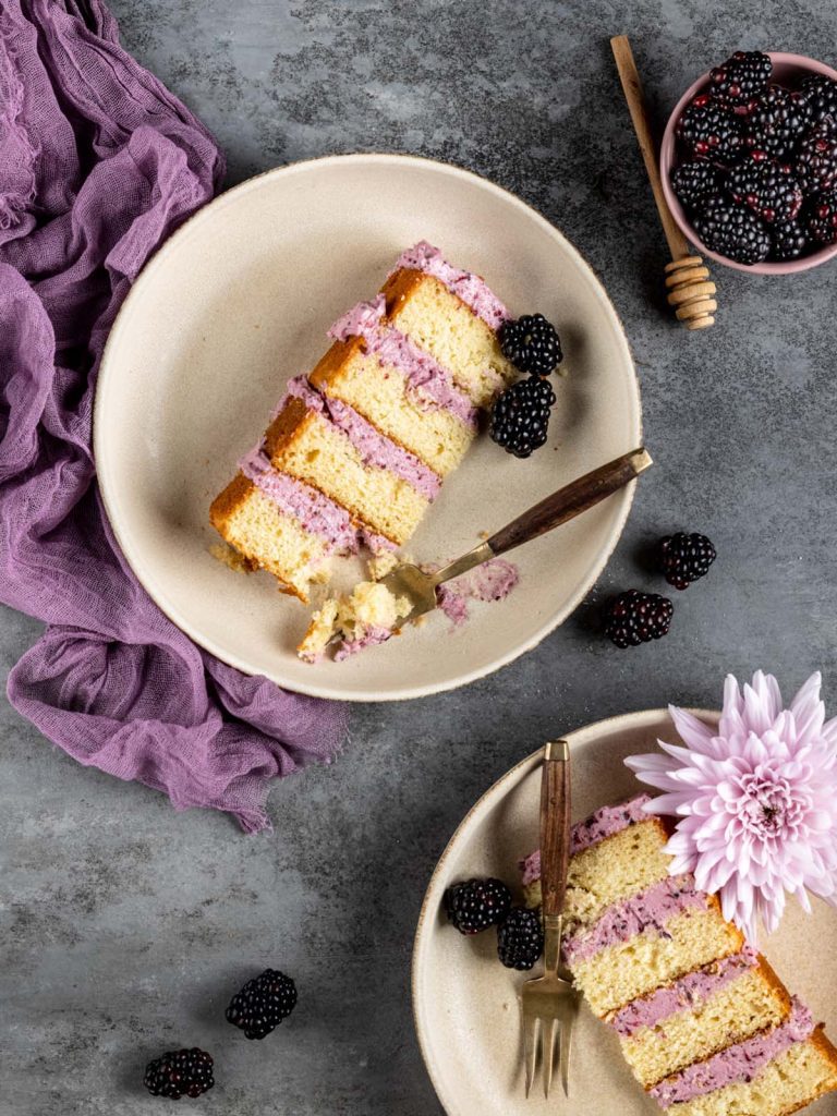 2 slices of cake on plates with forks and bowl of blackberries.