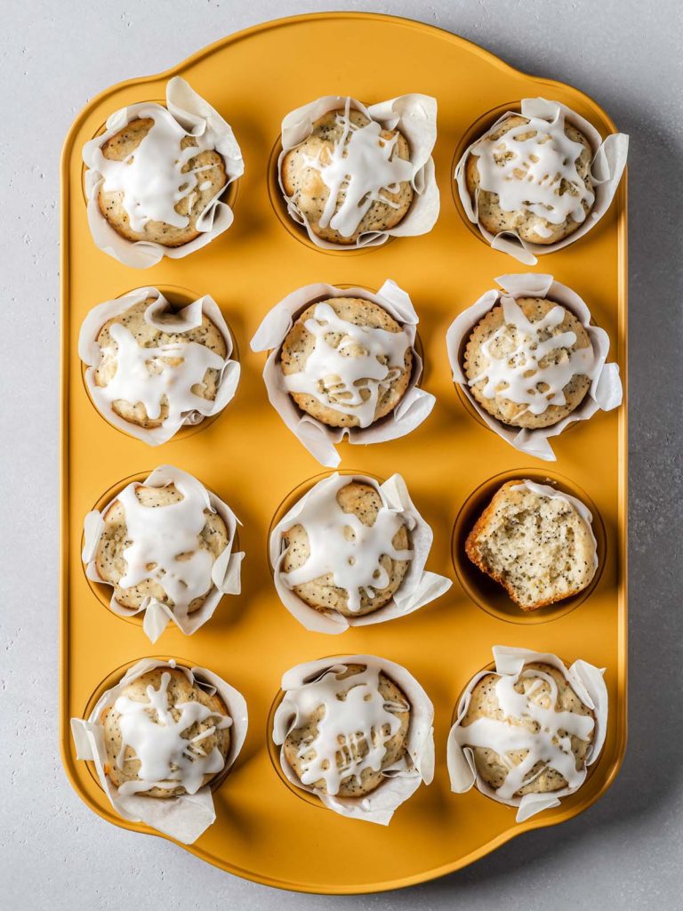Full yellow baking tray of muffins with one cut open.
