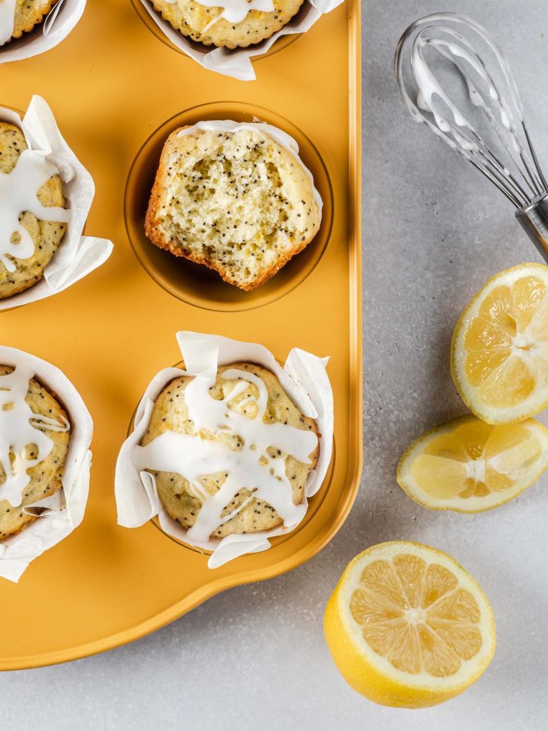 Close up of poppy seed muffins in yellow baking tray and sliced lemons.