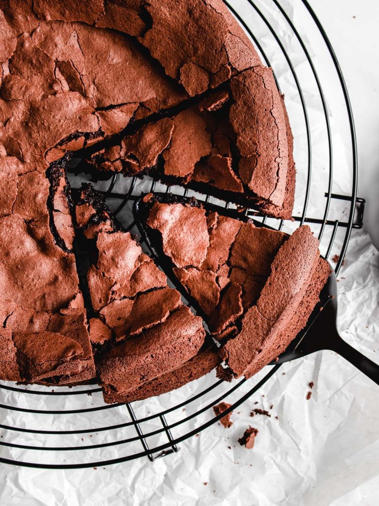 Removing slice from chocolate cake with spatula on cooling rack.