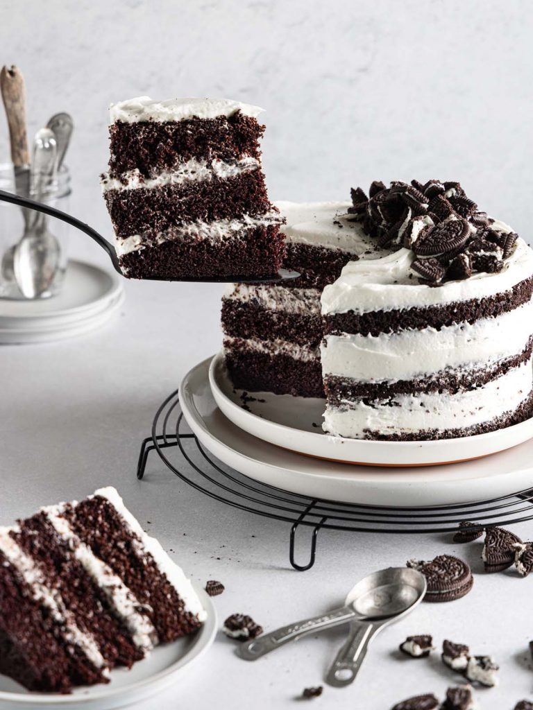 Removing slice of cake on cooling rack with one slice on plate in front.