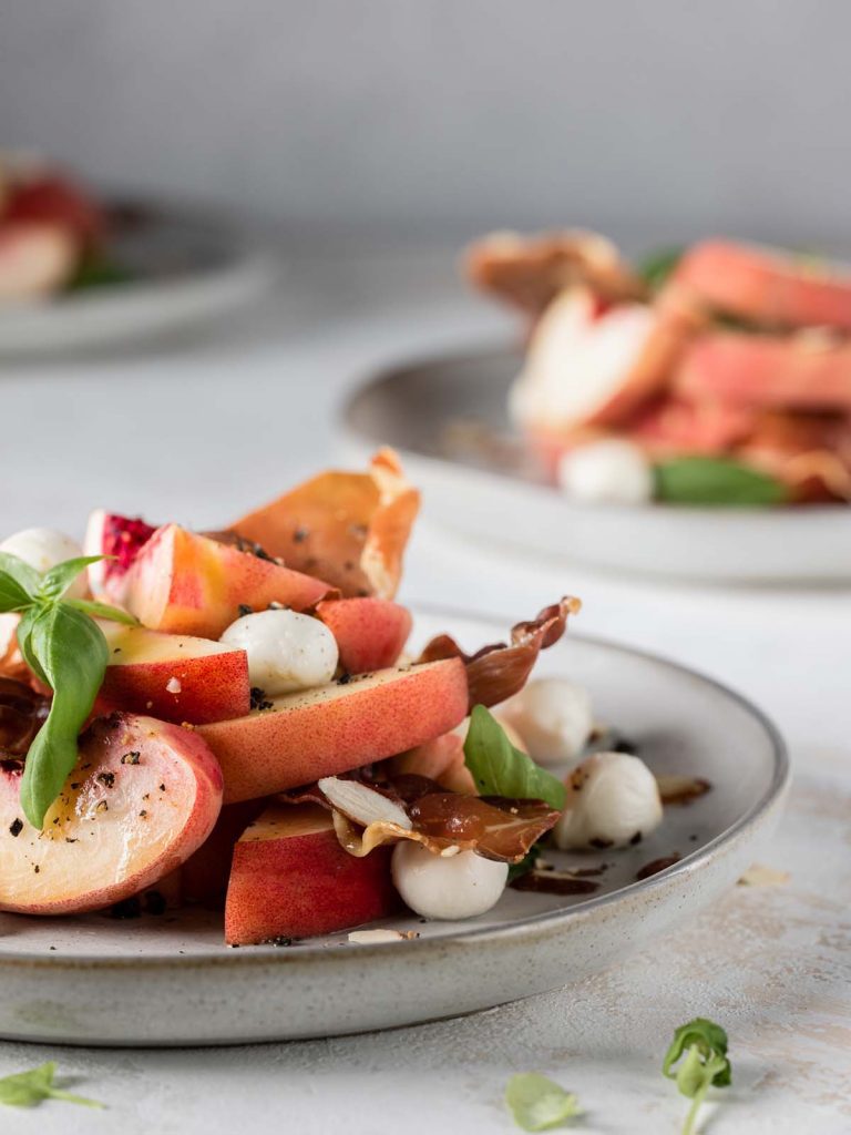 Salad on plate from the side with sliced peaches, mozzarella, and fresh basil leaves.