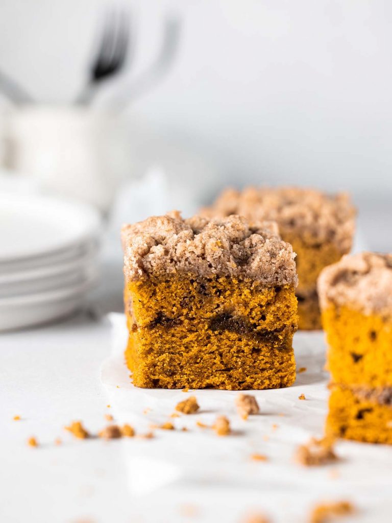 Slice of pumpkin cake sitting on parchment paper with slices and plates in the background.