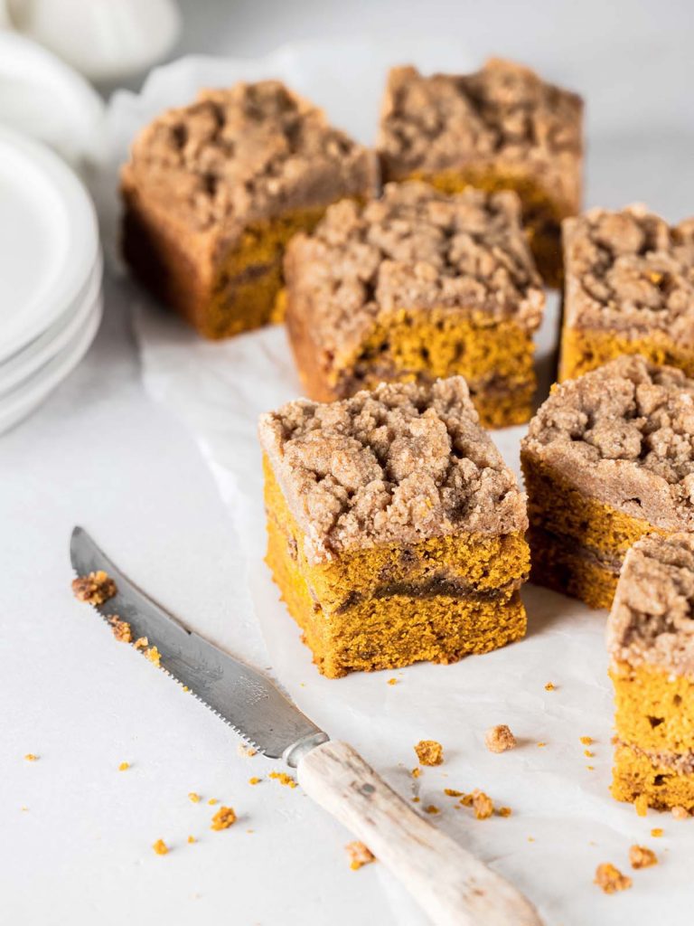 Row of coffee cake slices on parchment paper with knife and plates.