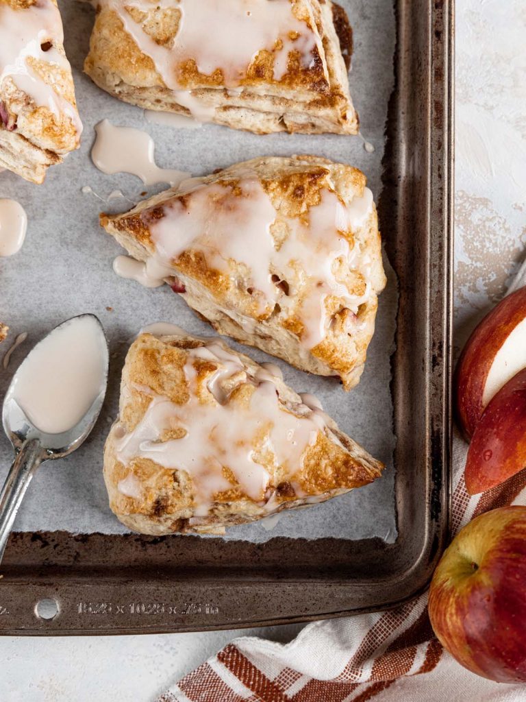 Close up on scones on sheet pan with spoon for drizzling glaze.