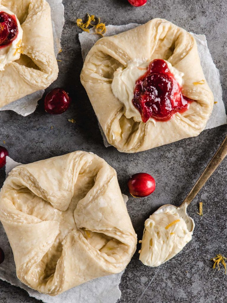 Close up of unbaked Danish with scoops of cream cheese and cranberry on top and spoonful of filling.