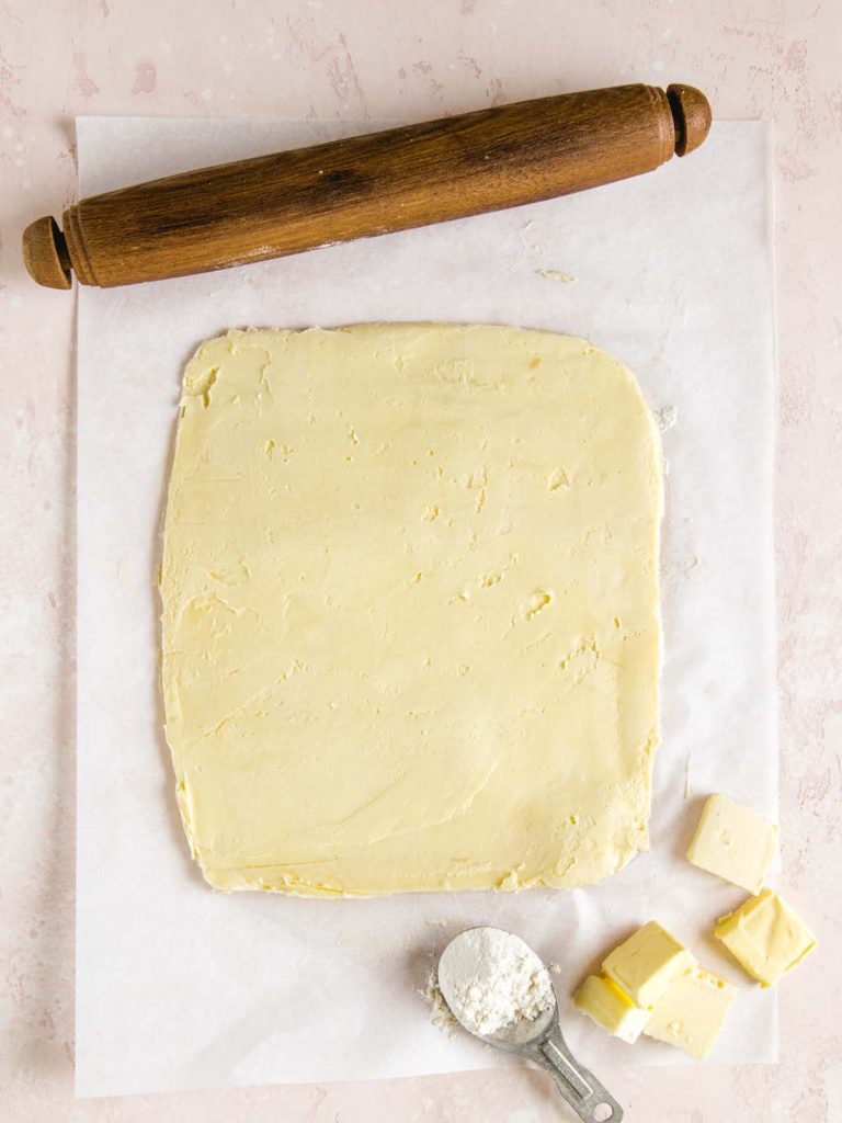 Sheet of butter on parchment paper with cubes of butter and scoop of flour.