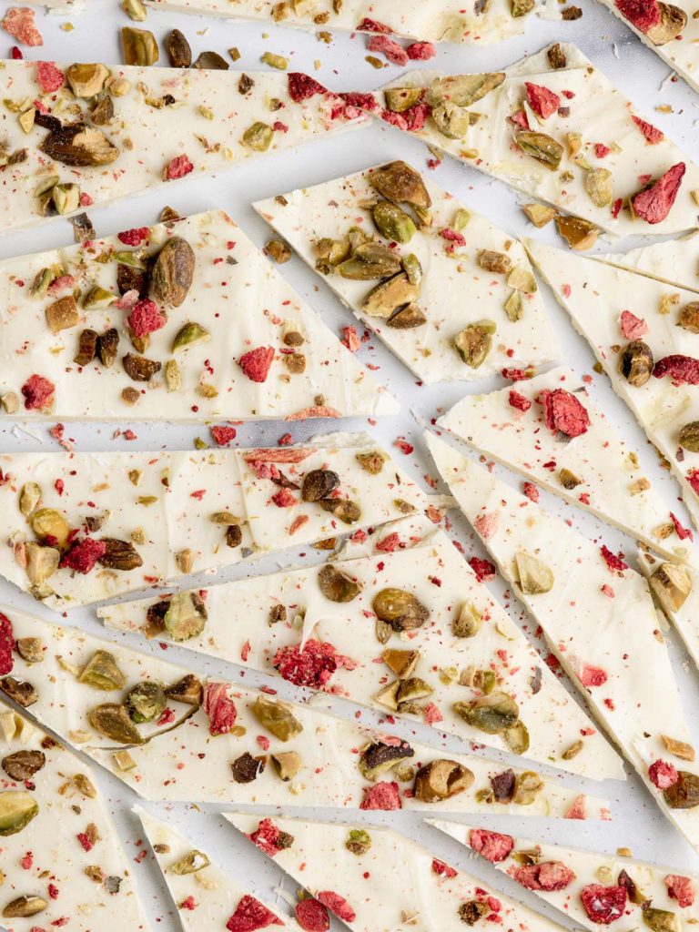 Close up of sliced white chocolate bark with chopped pistachios on bark with dried strawberries.