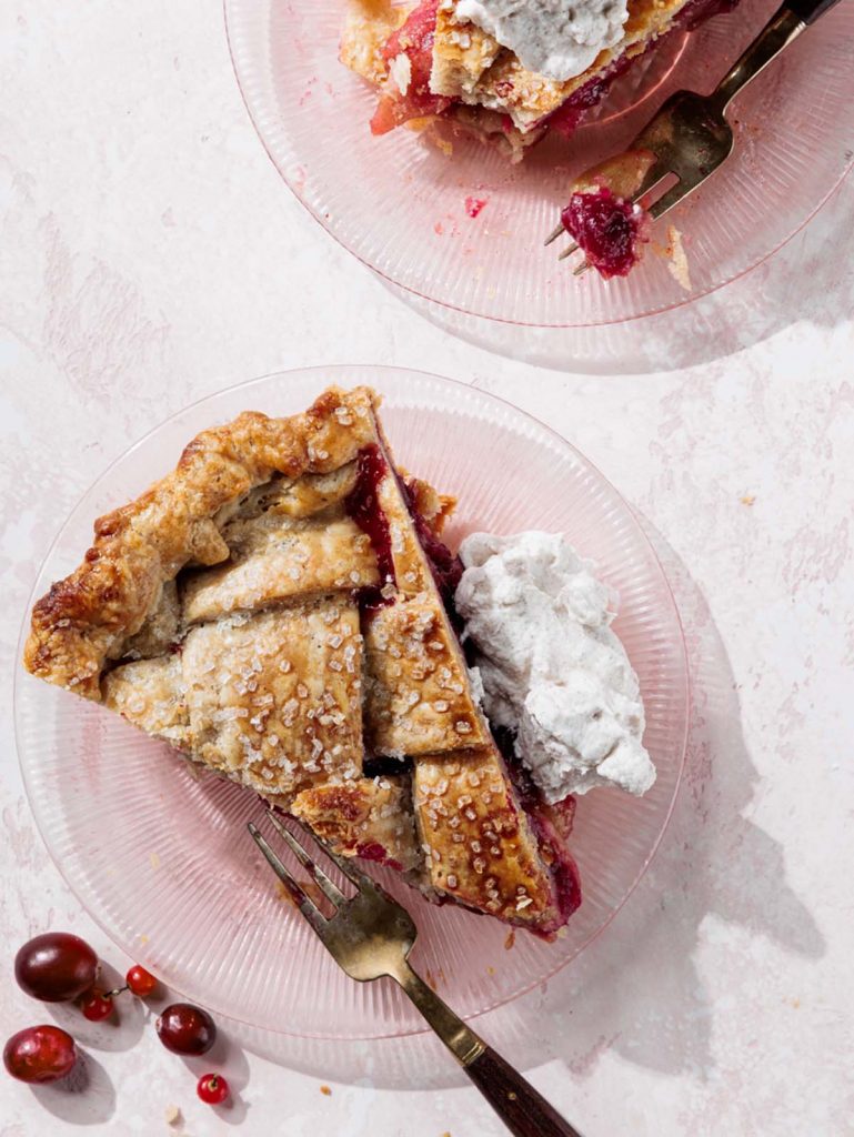 Two slices of pie on pink plates with forks and whipped cream.