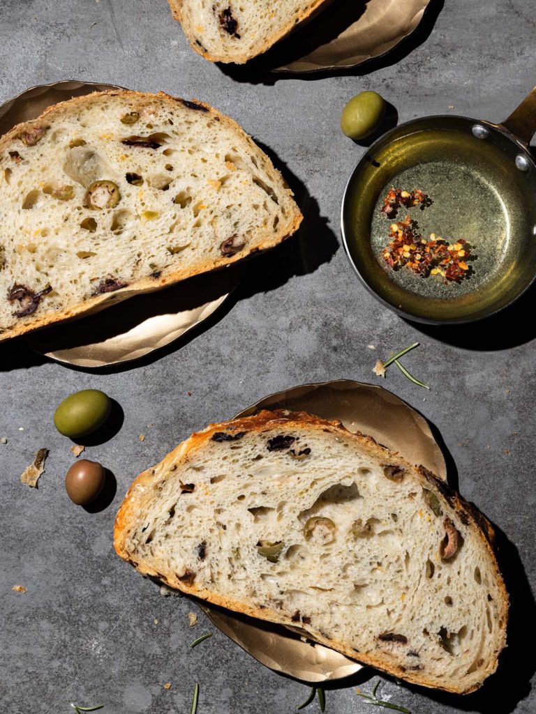 3 slices of olive bread on gold plates with dipping oil.