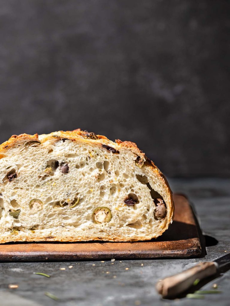 Slice of olive bread front view on cutting board with knife.