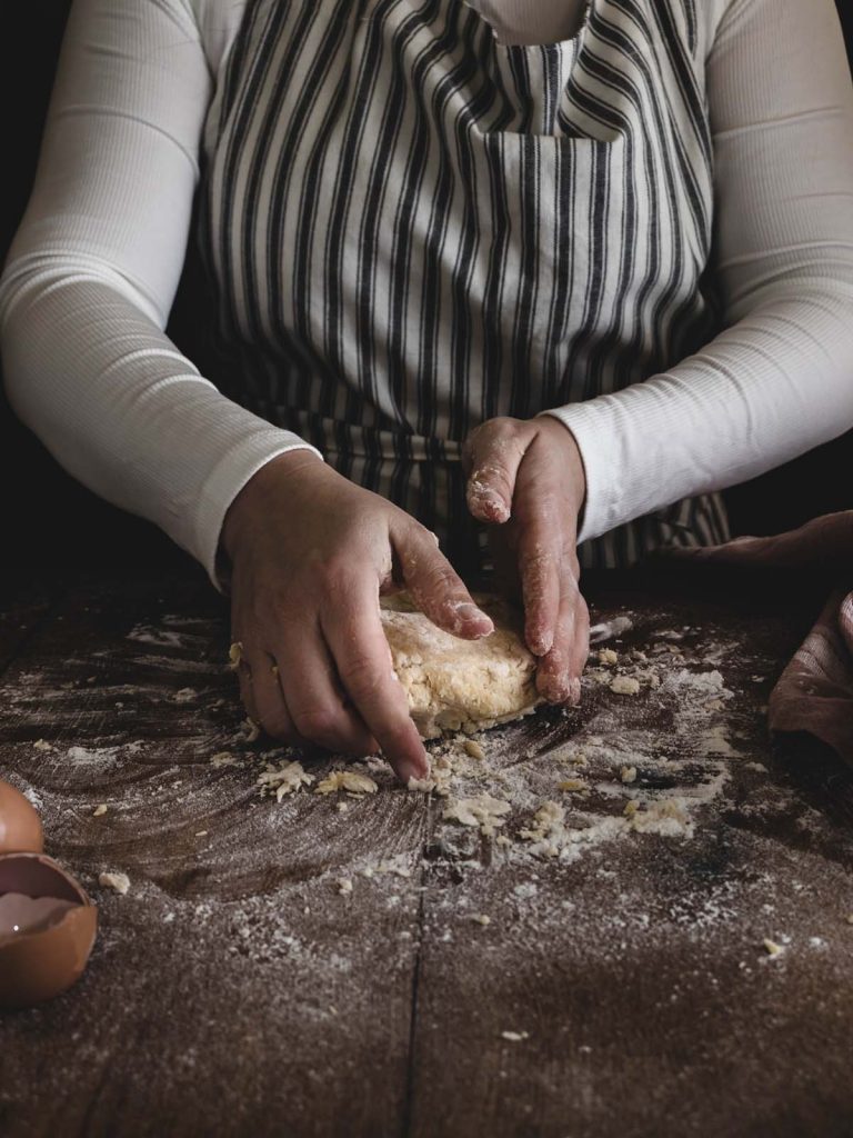 Chef kneading dough on flour covered board.