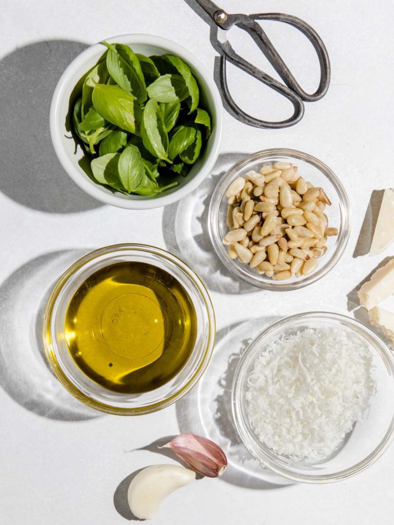 Pesto ingredients in small containers with scissors on board.