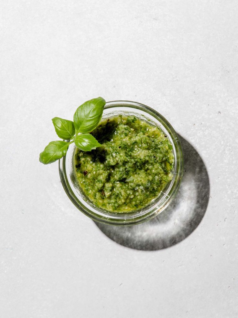 Small dish of Pesto Sauce in glass bowl with fresh basil leaves.