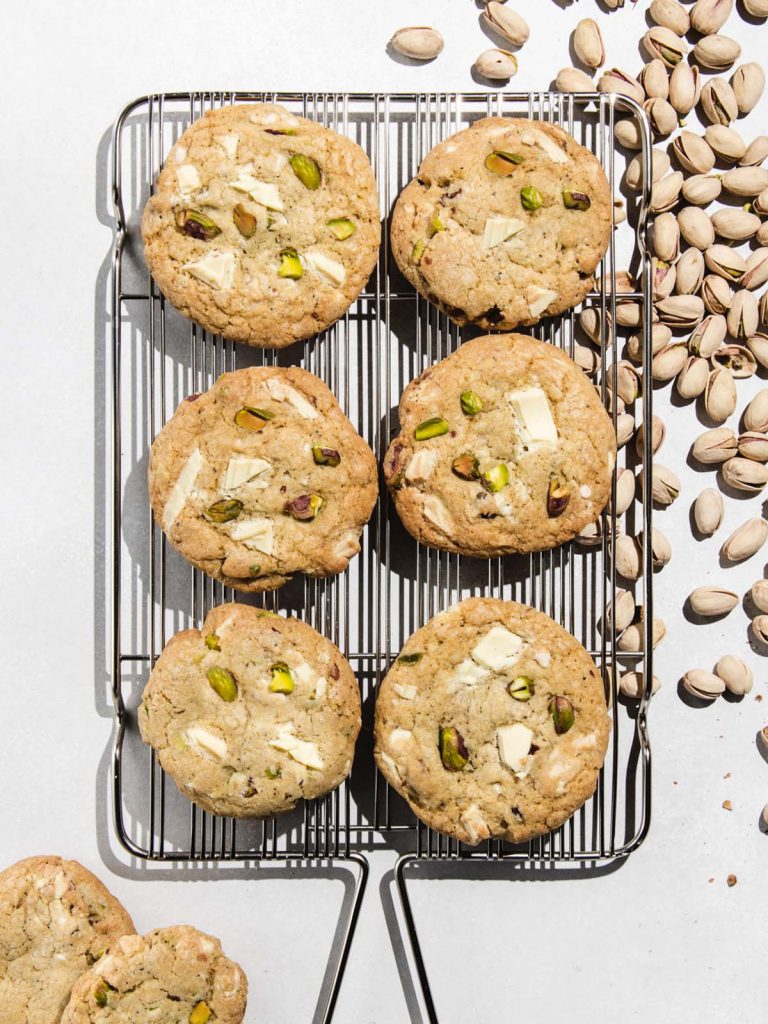 6 cookies on cooling rack with shelled pistachios on board.