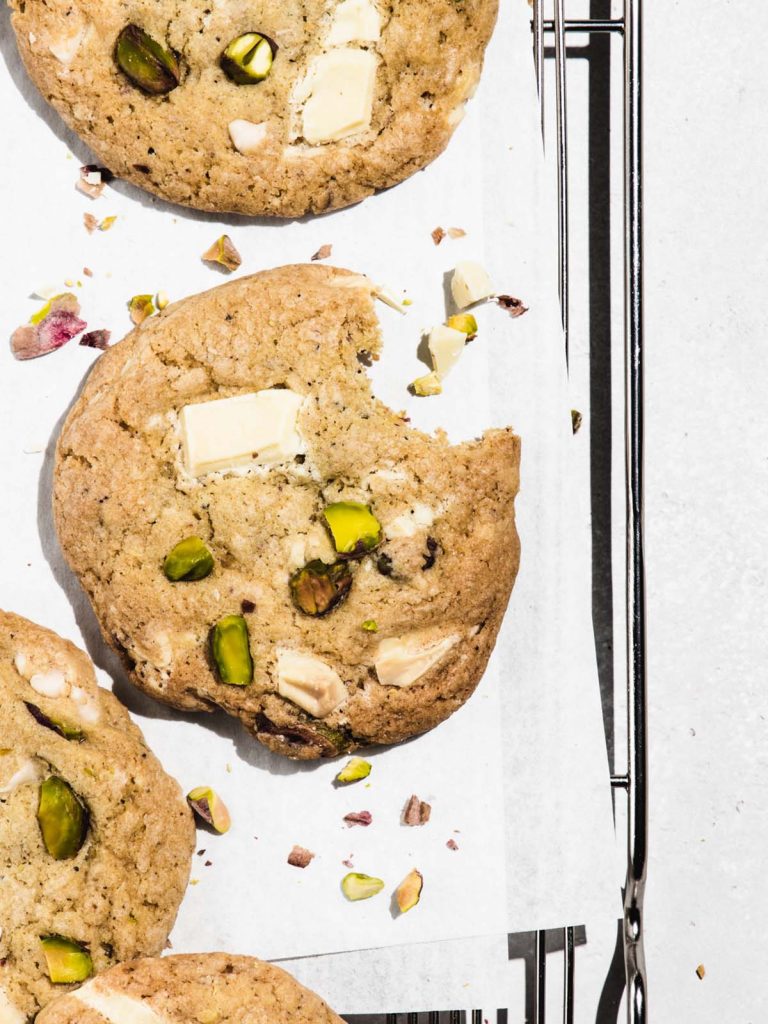 Close up of cookies with bite removed on cooling rack with chopped pistachios scattered.