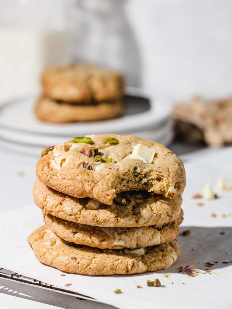 Stack of 4 cookies on parchment with scattered chopped pistachios and cookies on plates in background.
