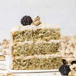 Slice of 3 layer pistachio cake on pie server with blackberries.