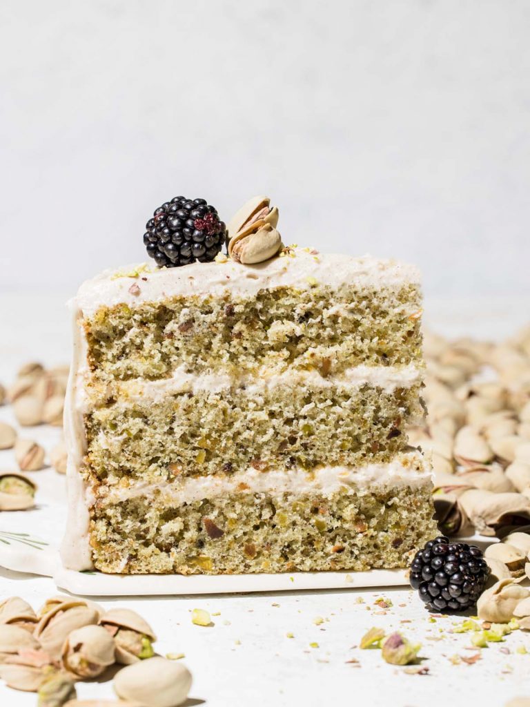 Three layer pistachio cake on cake server with blackberry on top.