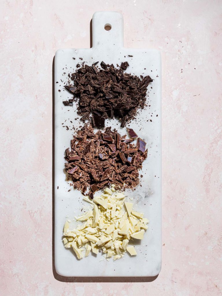 Three types of chocolate chopped on marble cutting board.