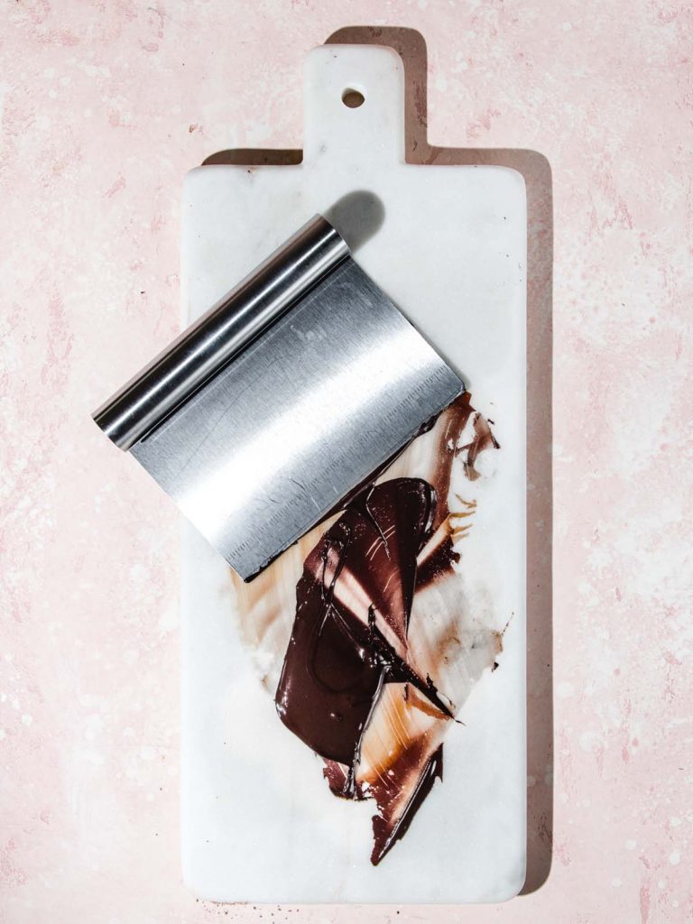 Melted chocolate on marble slab with bench scraper.