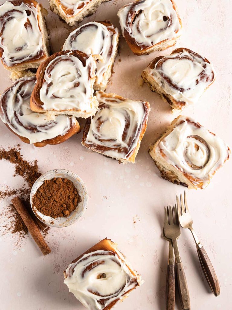 Cinnamon rolls placed across pink board with cinnamon dish and several forks.