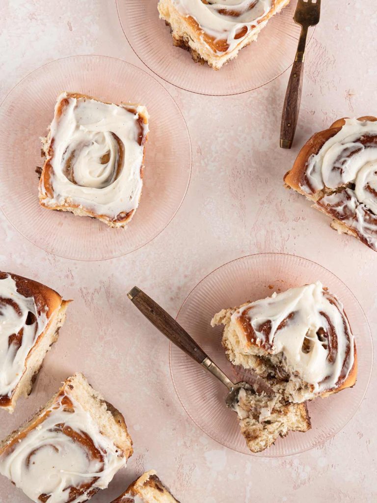 Cinnamon Rolls on pink plates with forks and rolls sitting on board.