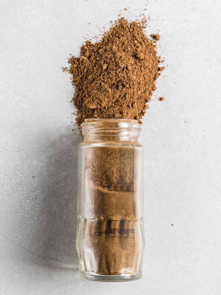 Jar of spice blend on side with spices spilling out.