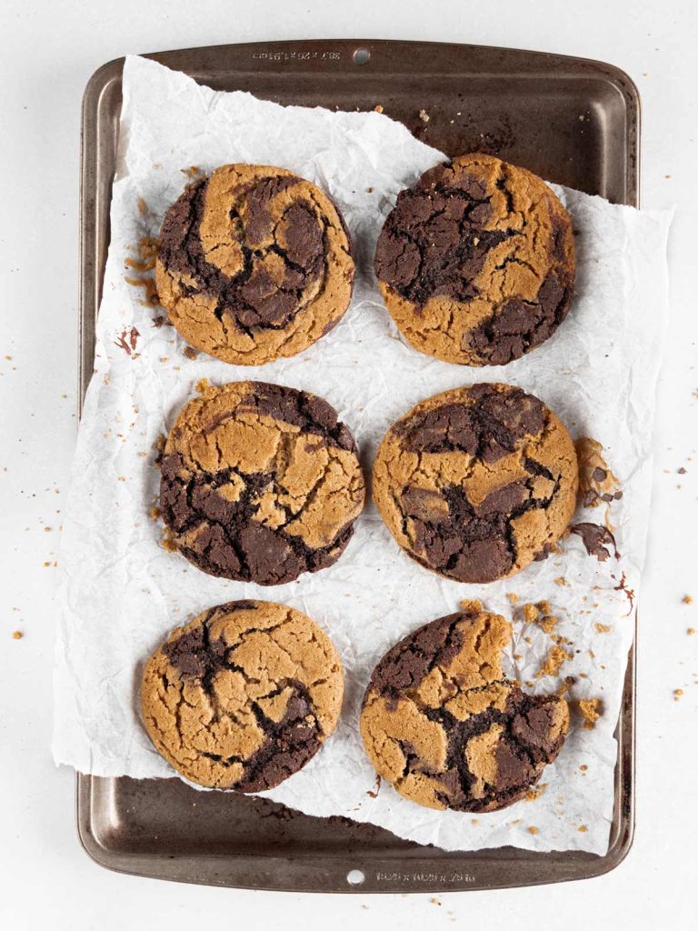 6 cookies on sheet pan with parchment paper with bite removed from one cookie.