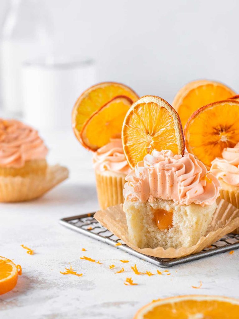 Cupcakes on cooling rack with dried orange slice decorations with bite removed from front cupcake.