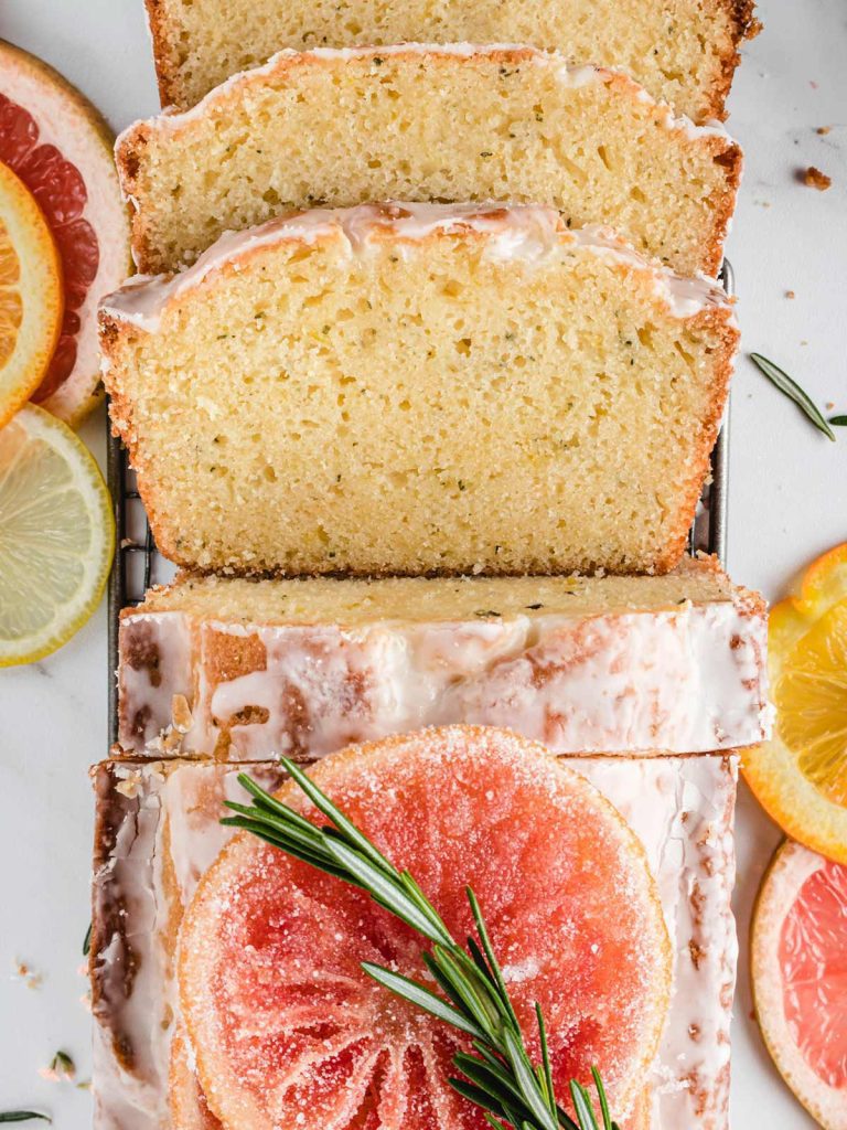 Sliced loaf cake overhead with spring of rosemary and candied grapefruit.