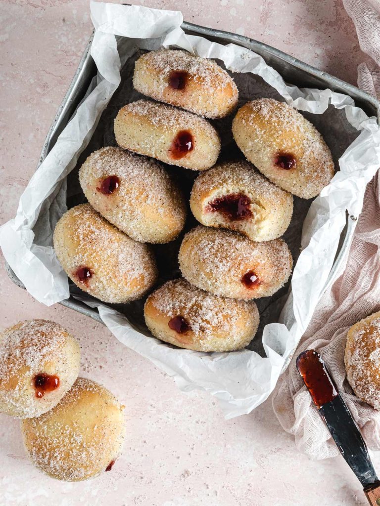 8 donuts in tin with 2 on the table with jellied spatula.