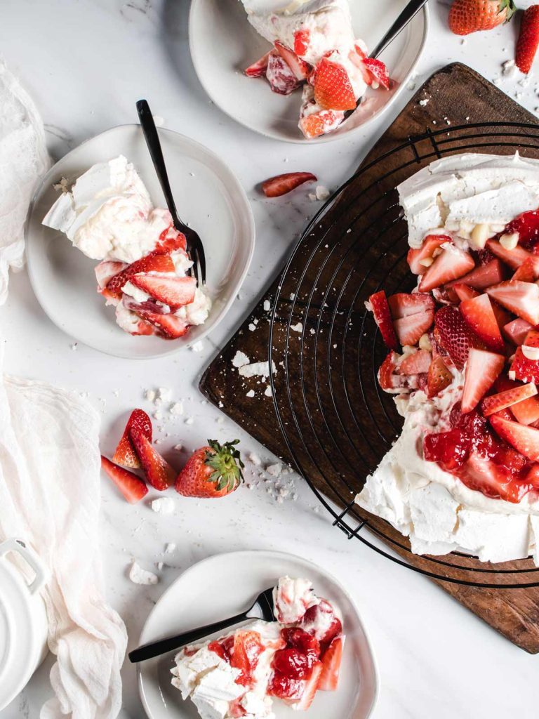 Slices of pavlova on plates with cascading sliced strawberries.