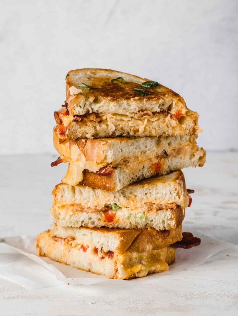 Stack of grilled cheese sandwiches cut in half on parchment paper.