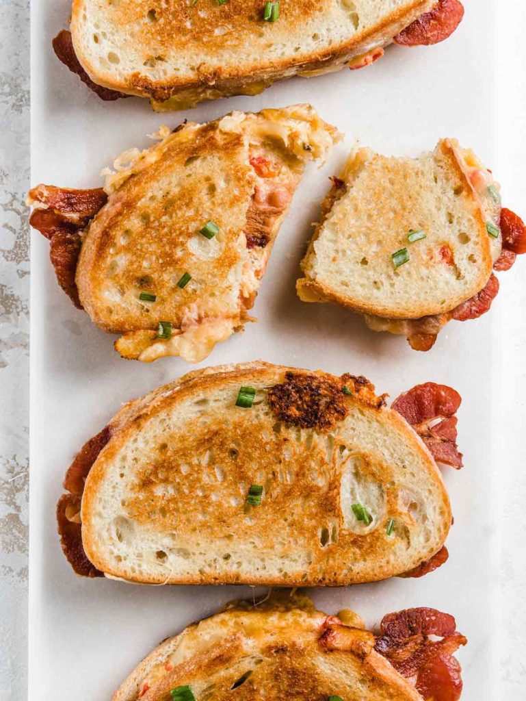 Grilled Cheese sandwiches on marble board with one sliced in half and bacon spilling out.