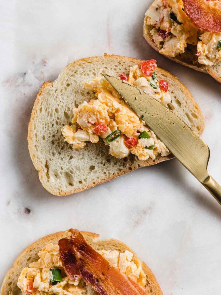 Smearing pimento cheese on bread with gold knife.