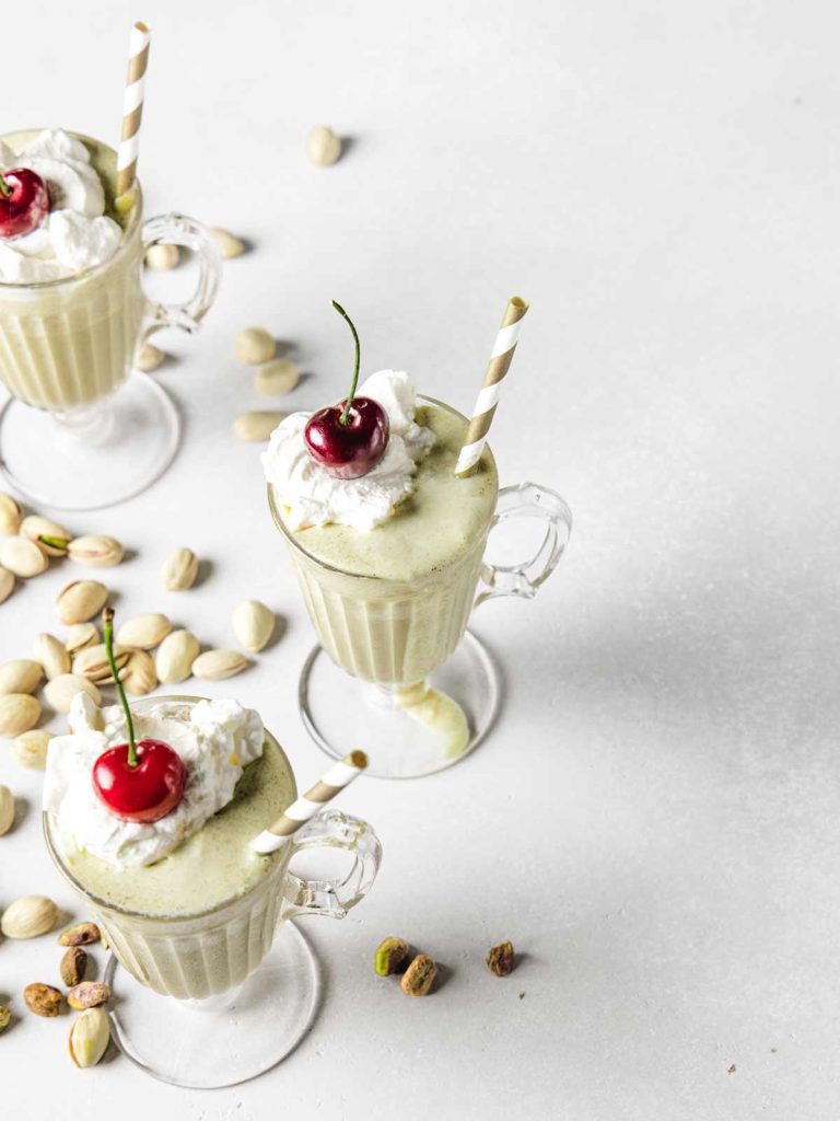 3 green milkshakes from above with whipped cream and cherries on top.