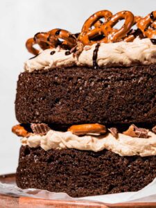 Close up of the side of chocolate layer cake with pretzels on top and drizzled chocolate.