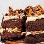 Removing slice of 2 layer chocolate cake with pretzels on top.