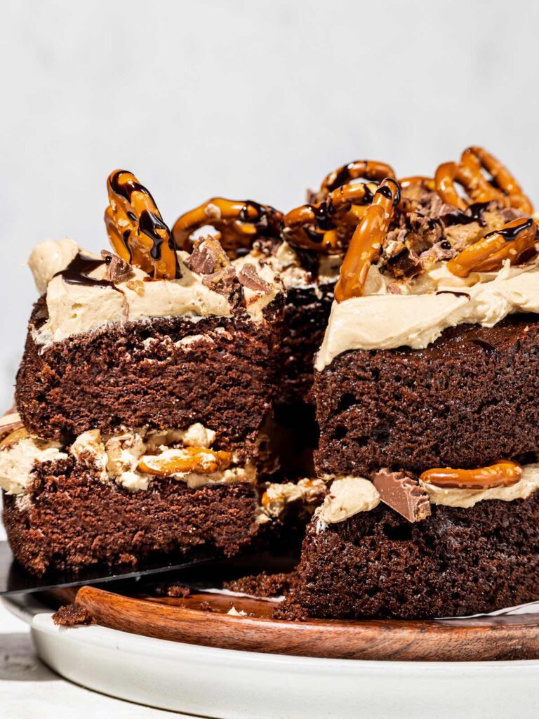 Removing slice of 2 layer chocolate cake with pretzels on top.