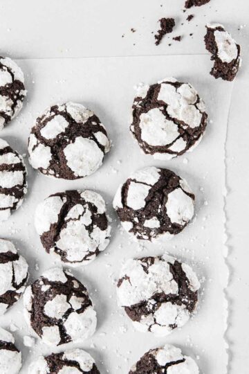 Chocolate cookies on parchment with crumbs and powdered sugar.