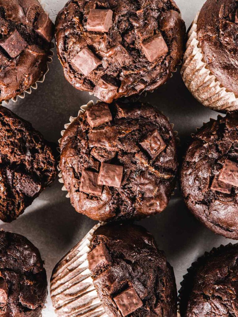 Close up of 9 muffins on board with chunks of chocolate and zucchini.