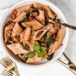 Skillet of rigatoni pasta with serving spoon and forks on the side.