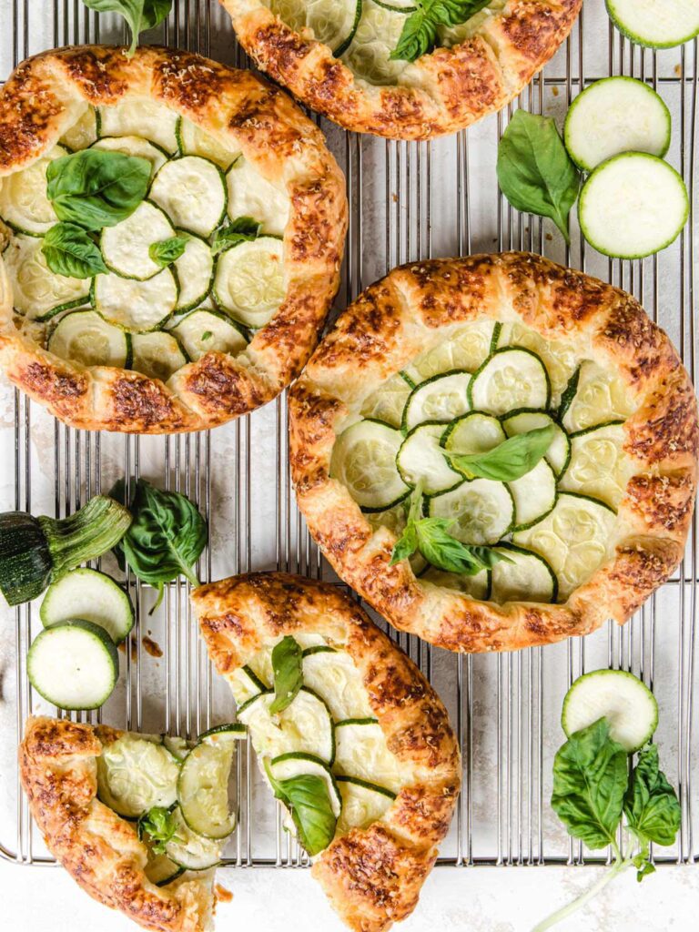 Four galettes on cooling rack with zucchini slices and fresh basil.